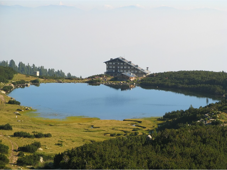 Хижа в планината, зелена растителност и езеро.